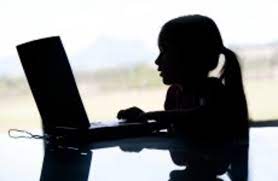 Dziewczynka siedzi przy stole i korzysta z laptopa. Komputer i dziewczynka są koloru czarnego
