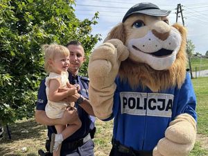 Policjant trzyma na rękach dziecko, a obok stoi Komisarz Lew