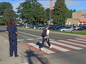 Policjantka stoi przy przejściu dla pieszych. Przed przejście przechodzi chłopiec.