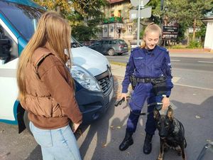 Jedna uczennica rozmawia z policjantką, która jest przewodnikiem pas służbowego, obok nich siedzi suczka o imieniu Rata - owczarek niemiecki.