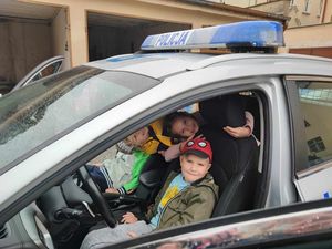 Dzieci siedzą w radiowozie policyjnym i się uśmiechają.
