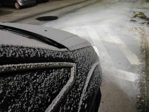 Przód samochodu pokryty śniegiem, na drodze znajduje się mała warstwa śniegu