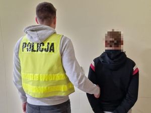 Zdjęcie przedstawia dwóch mężczyzn stojących tyłem do zdjęcia. Po prawej stronie znajduje się policjant nieumundurowany ubrany w kamizelkę odblaskową z napisem Policja, obok niego stoi mężczyzna w bluzie.