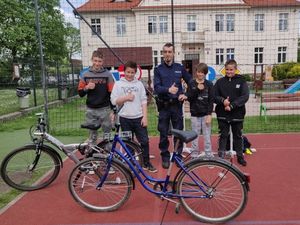 Zdjęcie przedstawia policjanta, który stoi wraz z uczniami którzy będą zdawać egzamin na kartę rowerową