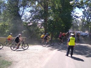 Zdjęcie przedstawia policjanta stojącego tyłem zabezpieczającego przejazd rowerzystów