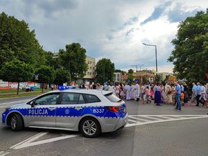 Zdjęcie przedstawia radiowóz oznakowany oraz policjantów zabezpieczających procesje na ulicy Trzebnicy