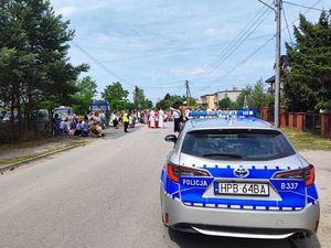 Zdjęcie przedstawia policjantów zabezpieczających procesje, widać również tył radiowozu oznakowany