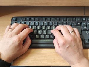 Zdjęcie przedstawia klawiaturę komputerową oraz dwie ręce