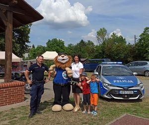 Zdjęcie przestawia policjanta wraz z kobietą, dwójką chłopców oraz maskotka dolnośląskiej Policji komisarzem Lwem. Wszyscy stoją na tle radiowozu