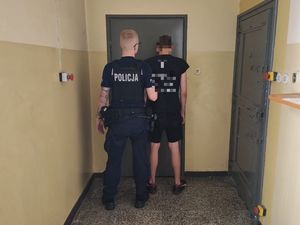 Na zdjęciu stoją dwie osoby tyłem, policjant ubrany w mundur oraz zatrzymany nieletni