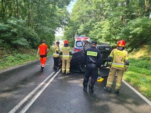 Na miejscu zdarzenia pracują służby, tyłem stoją funkcjonariusze straży pożarnej w tle widać również pogotowie ratunkowe