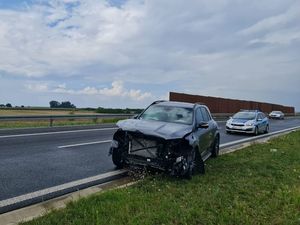 Na zdjęciu widoczny jest samochód biorący udział w zdarzeniu drogowy, który posiada uszkodzony przód w tle widać radiowóz policyjny