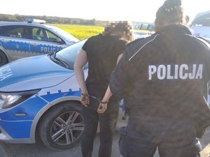 Zatrzymana kobieta ma założone kajdanki na ręce trzymane z tyłu. Soi wraz z policjantką przy radiowozie