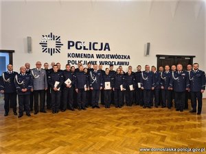 Wszyscy nowo przyjęci policjanci stoją przy ścianie z Komendantem Wojewódzkim Policji we Wrocławiu oraz Komendantami Powiatowymi. Na ścianie napis Komenda Wojewódzka Policji we Wrocławiu