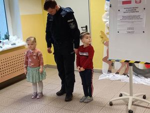 Policjant, a obok niego stoi mała dziewczynka i chłopiec