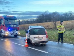 Uszkodzony pojazd osobowy, uszkodzony tył, obok stoi pojazd straży pożarnej oraz strażak