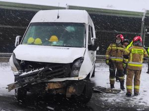 Uszkodzony pojazd typu bus z uszkodzonym przodem obok niego znajdują się strażacy