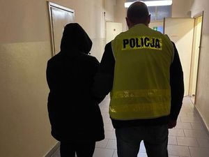 Sprawca stoi obok policjanta ubranego w kamizelkę odblaskową z napisem Policja