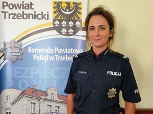 Dzielnicowa miasta Trzebnica sierżant sztabowy Katarzyna Brożyna. Policjantka stoi obok baneru Komendy Powiatowej Policji w Trzebnicy, ubrana w koszulę z krótkim rękawem.