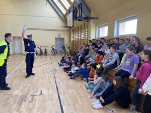 Policjant ruchu drogowego omawia sygnalizację i pokazuje dzieciom co oznaczają znaki wydawane przez policjantów.