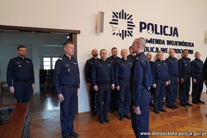 Prowadzący uroczystość składa meldunek Komendantowi Wojewódzkiemu Policji we Wrocławiu. Spotkanie odbywa się w sali komendy. Policjanci stoją na baczność.