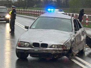 Uszkodzone auto, które jest holowane. Drogę zabezpiecza policjant umundurowany.