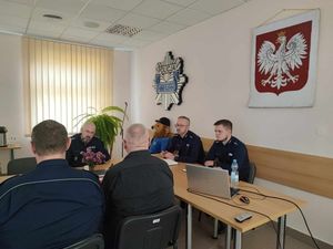 przy stole siedząą umundurowaniu funkcjonariusze policji