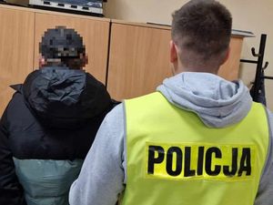 Zatrzymany wraz z policjantem kryminalnym, który ma założoną kamizelkę odblaskową z napisem Policja stoją tyłem do zdjęcia.