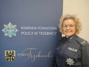 Policjantka ubrana w mundur służbowy. Soi przy banerze Komendy Powiatowej Policji w Trzebnicy