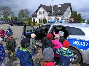 Dzieci zwiedzają oznakowany radiowóz policyjny na terenie przy szkole.