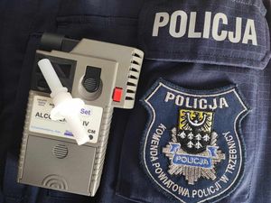 Urządzenie do badania stanu trzeźwości leży na policyjnej kurtce, na której znajduje się napis Komenda Powiatowa Policji w Trzebnicy oraz logo powiatu