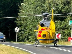 Lotnicze Pogotowie Ratunkowe - helikopter stoi na środku drogi dwukierunkowej, drogę zabezpiecza oznakowany radiowóz policyjny