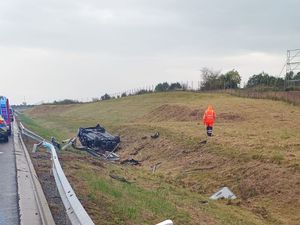 Zdjęcie przedstawia pobocze drogi ekspresowej S5, gdzie w przydrożnym rowie na dachu leży samochód osobowy. Niebo jest zachmurzone. Z lewej strony widać fragment oznakowanego radiowozu policji oraz straży pożarnej.