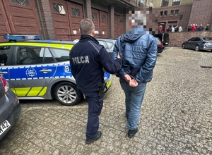 prowadzony przez policjant zatrzymany mężczyzna w kajdankach