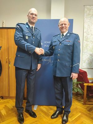 Komendant Powiatowy Policji w Trzebnicy oraz policjant zmieniający stanowisko stoją w pokoju obok siebie. Oboje ubrani w mundury galowe