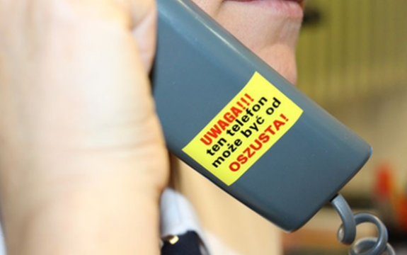 Zdjęcie przedstawia osobę, która przy twarzy trzyma słuchawkę od telefony stacjonarnego.