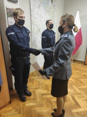Na zdjęciu I zastępca Komendanta Powiatowego Policji w Trzebnicy wręcza nowo przyjętemu policjantowi akt ślubowania, który znajduje się w teczce z logiem komendy.