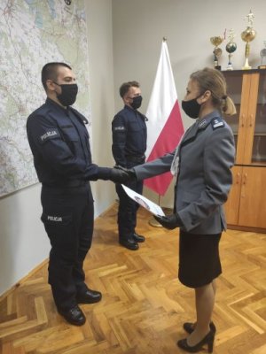 Na zdjęciu I zastępca Komendanta Powiatowego Policji w Trzebnicy wręcza nowo przyjętemu policjantowi akt mianowania, który znajduje się w teczce z logiem komendy.